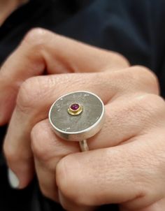 "This is a silver concrete ring. Handmade ring made of 925 silver, its surface is round which has been covered with gray concrete and in the center it has a red ruby bound with solid 14 carat gold. Its finish is slightly rough. It is a special ring that combines different materials. In contact with skin, moisture and air, concrete becomes darker. DESCRIPTIONS and MEASUREMENTS: Material:Sterling silver, 14k  gold. Surface: Concrete Gem :Ruby 0,2 (cm) 0,08 (in\"). Diameter disc: 2,0 (cm) 0,78 (in\") thickness 0,4 (cm) 0,16 (in\"). SEE MORE CONCRETE RINGS HERE: www.etsy.com/shop/ArtisJewels?ref=shop-header-name&listing_id=1423833226&from_page=listing&search_query=concrete+rings Visit my Etsy shop, ArtisJewels, to see more rings and jewelry and other unique handmade pieces. www.etsy.com/shop/A Concrete Ring, Gem Ruby, Gray Concrete, Contemporary Ring, Special Ring, Gold And Silver Rings, Silver Rings Handmade, Red Ruby, Ring Handmade