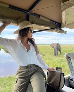 a woman standing on the back of a vehicle in front of an elephant and another animal