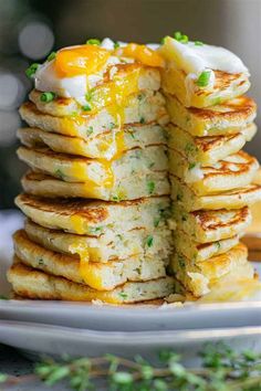 a stack of pancakes with eggs on top and chives around the edges, stacked on a white plate