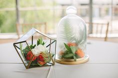 two small glass vases with flowers in them on top of a white table cloth