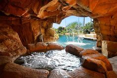 an outdoor hot tub in the middle of a pool surrounded by large rocks and boulders