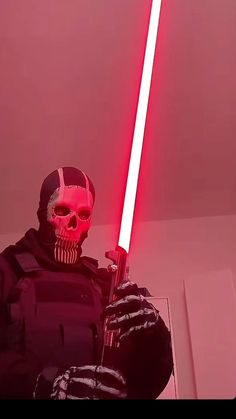 a man with a red light saber standing in front of a pink wall wearing a skull mask