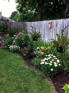 a garden filled with lots of flowers next to a wooden fence in the middle of a yard