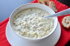 a white bowl filled with soup next to slices of bread on a red napkin and knife