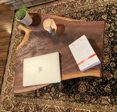 a wooden table topped with a laptop computer next to a book and plant on top of it