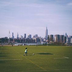 a person on a field with a soccer ball in front of the cityscape