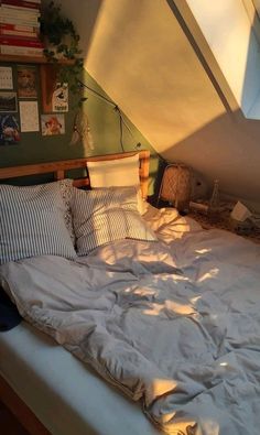 an unmade bed with white sheets and pillows in a loft space under a slanted ceiling