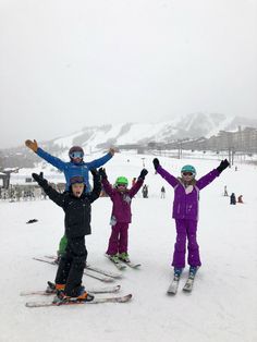 three children standing on skis in the snow with their arms up and hands raised