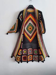 a colorful crocheted coat hanging on a white wall next to a hanger