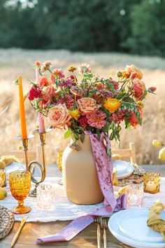 a vase filled with flowers sitting on top of a wooden table next to plates and candles