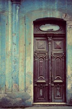 an old wooden door with a clock on the top and bottom panel, in front of a blue wall