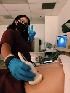 a woman in blue gloves and face mask standing next to a monitor with an x - ray on it