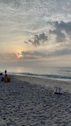 two people sitting on the beach watching the sun rise over the water and clouds in the sky