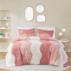 a bed with pink and white comforters in a bedroom area next to two round mirrors on the wall