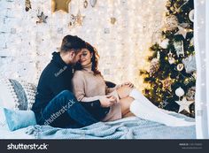 a man and woman sitting on a bed in front of a christmas tree with lights