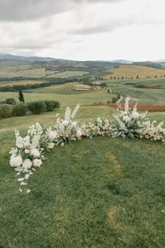 an outdoor ceremony setup with white flowers and greenery on the grass, overlooking rolling hills