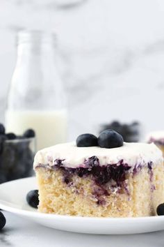 a piece of blueberry cake on a white plate next to a glass of milk