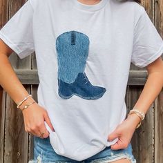 a woman standing in front of a wooden fence wearing a white shirt with a cowboy boot on it