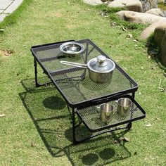 an outdoor table with two pots and pans on it in the grass next to some rocks