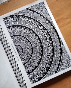 a spiral notebook with black and white designs on it sitting on top of a wooden table