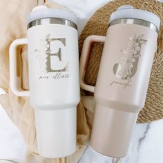 two travel mugs sitting next to each other on top of a table with a straw bag