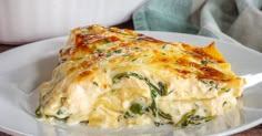 a white plate topped with a cheesy casserole covered in cheese and spinach