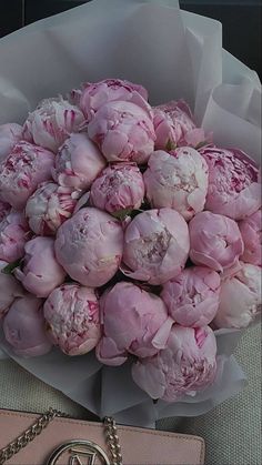 a bouquet of pink peonies in front of a handbag on a table