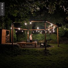 a man sitting at a picnic table in the middle of a yard with string lights strung across it