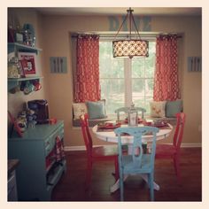 a dinning room table and chairs in front of a window with red drapes