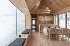 a kitchen and dining area in a wooden house with large windows overlooking the snow covered field