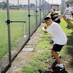 a man holding a baseball bat while standing next to a fence with other people behind him