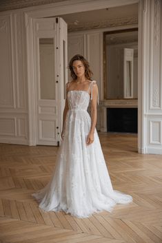 a woman in a white wedding dress standing on a wooden floor with an open door