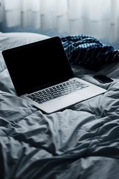 an open laptop computer sitting on top of a bed in front of a white window