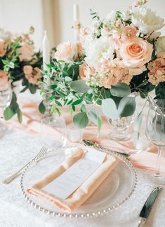 the table is set with pink and white flowers in vases, silverware, and napkins