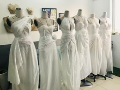 several white dresses on mannequins in front of a wall with pictures behind them