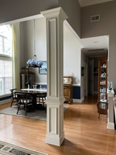 a living room with hardwood floors and white columns in the center, along with a dining table