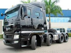 a large black semi truck parked in front of a building with palm trees behind it