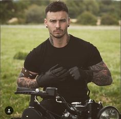 a man with tattoos on his arm sitting on a motorbike in the grass