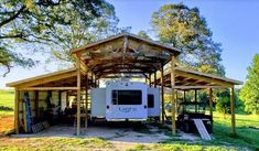 an rv is parked under a wooden structure in the grass with trees and other things around it