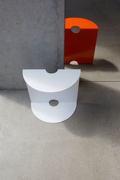 a white toilet sitting next to a red and orange trash can on cement flooring