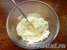 a glass bowl filled with whipped cream on top of a wooden table next to a metal spoon