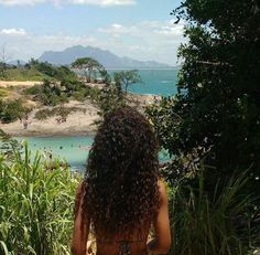 a woman with long curly hair is looking out over the water from a hill top