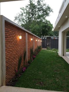 a brick wall with two lights on it next to a grassy area in front of a house