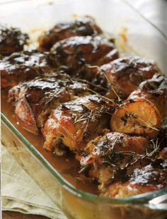 a glass dish filled with meat covered in sauce and garnished with fresh herbs