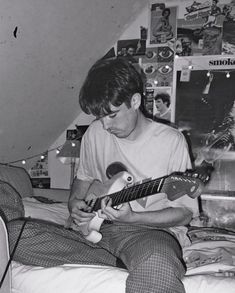 a man sitting on a bed playing an electric guitar