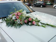 a bouquet of flowers on the hood of a white car in front of a city street