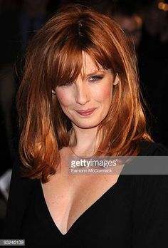 a woman with long red hair and black dress posing for the camera at an event