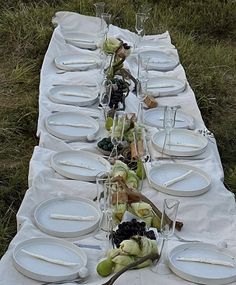 a long table is set with white plates and silverware for an outdoor dinner party