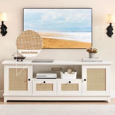 a white entertainment center with wicker baskets on the bottom and an art piece above it