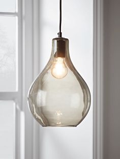 a glass light hanging from a ceiling in front of a white wall with windows and a window sill